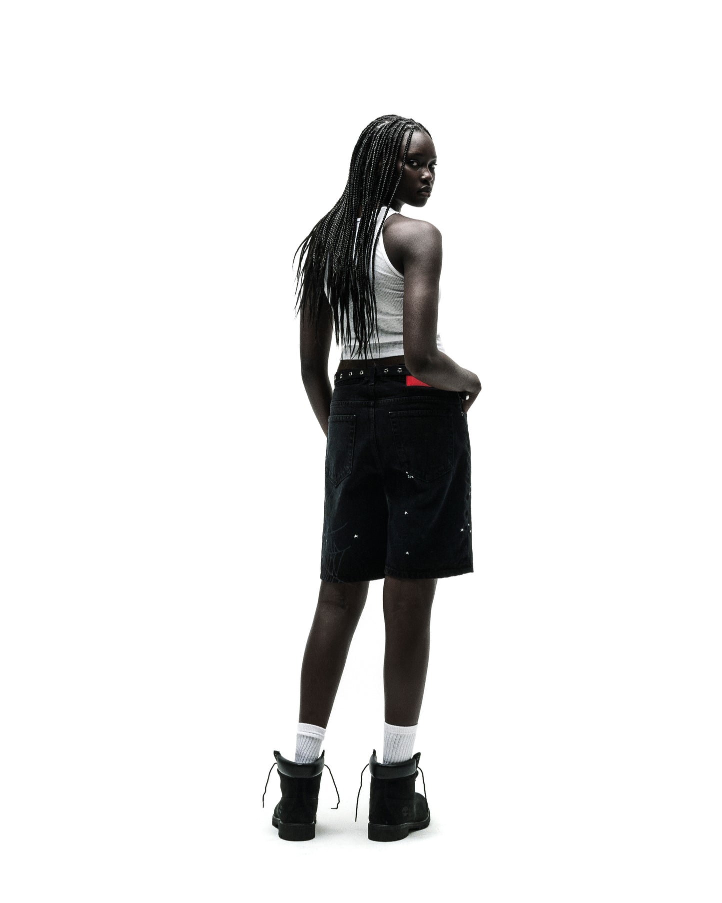 Woman in black HEAVY WEB JEAN SHORTS with white paint splatters, a white tank top, and black boots.