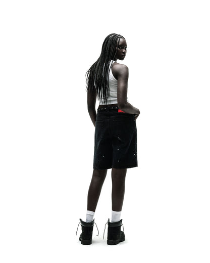Woman in black HEAVY WEB JEAN SHORTS with white paint splatters, a white tank top, and black boots.