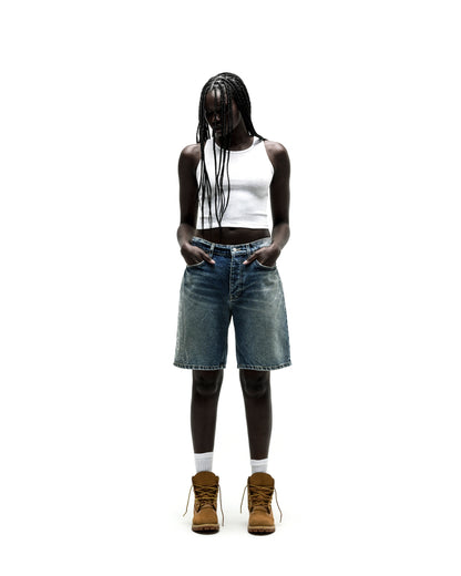 Model in vintage wash denim shorts with rhinestone web design, white tank top, and brown boots.