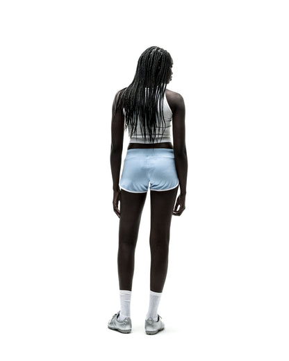Woman from behind wearing light blue SP5 Wide Boxer shorts with white trim, white crop top, and silver sneakers.