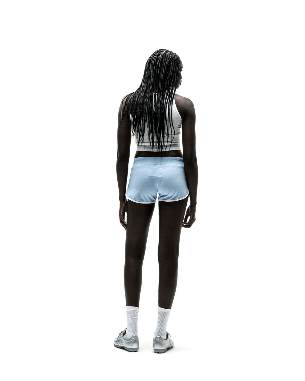 Woman from behind wearing light blue SP5 Wide Boxer shorts with white trim, white crop top, and silver sneakers.