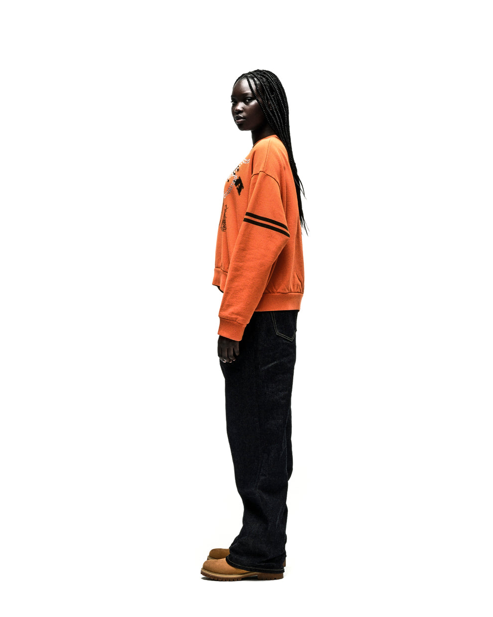 Aranea Crewneck: Orange oversized sweatshirt with black arm stripes, worn by a model in dark jeans.