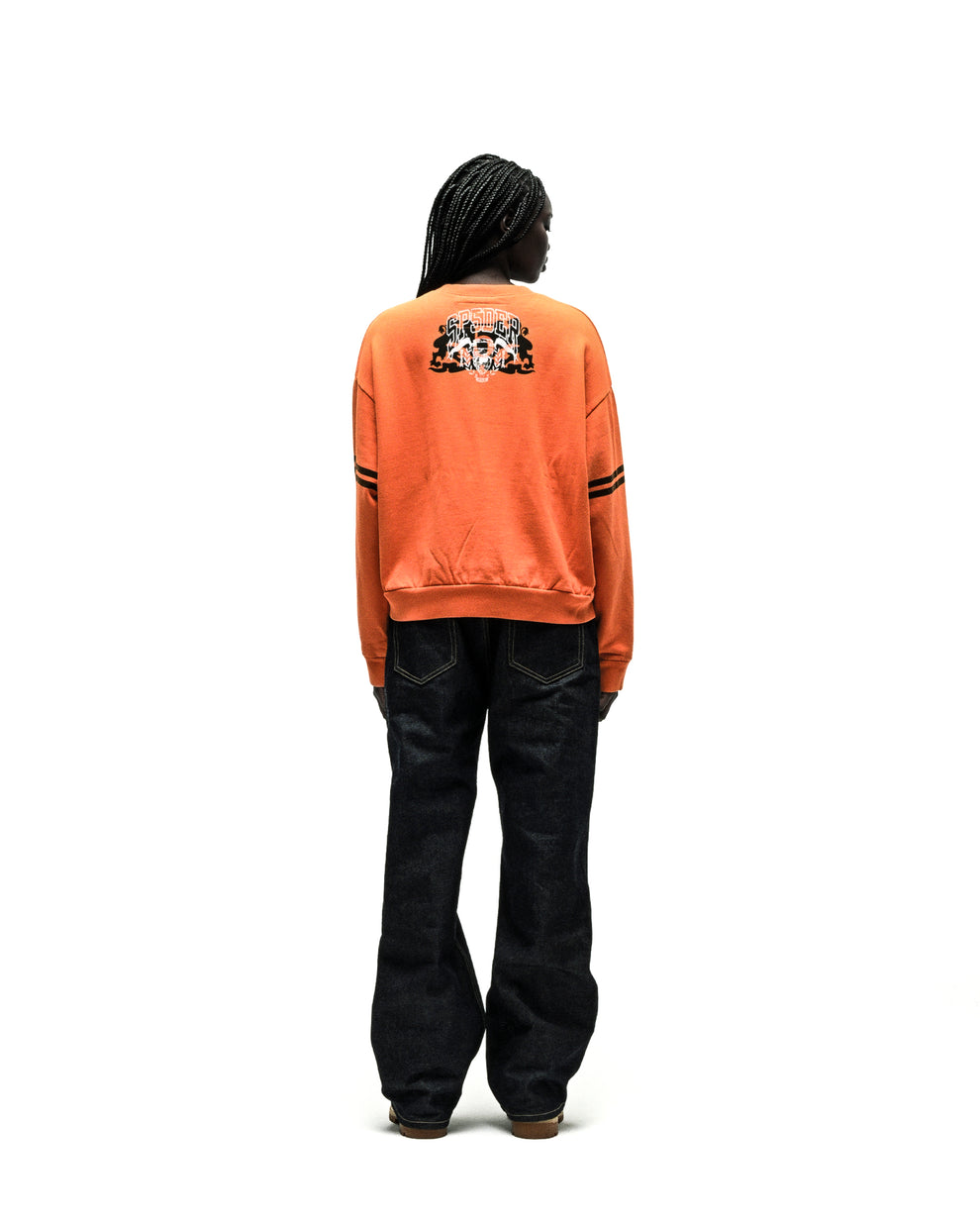 ARANEA CREWNECK: Orange sweatshirt with black graphic on back, black stripes on sleeves, dark wash jeans.