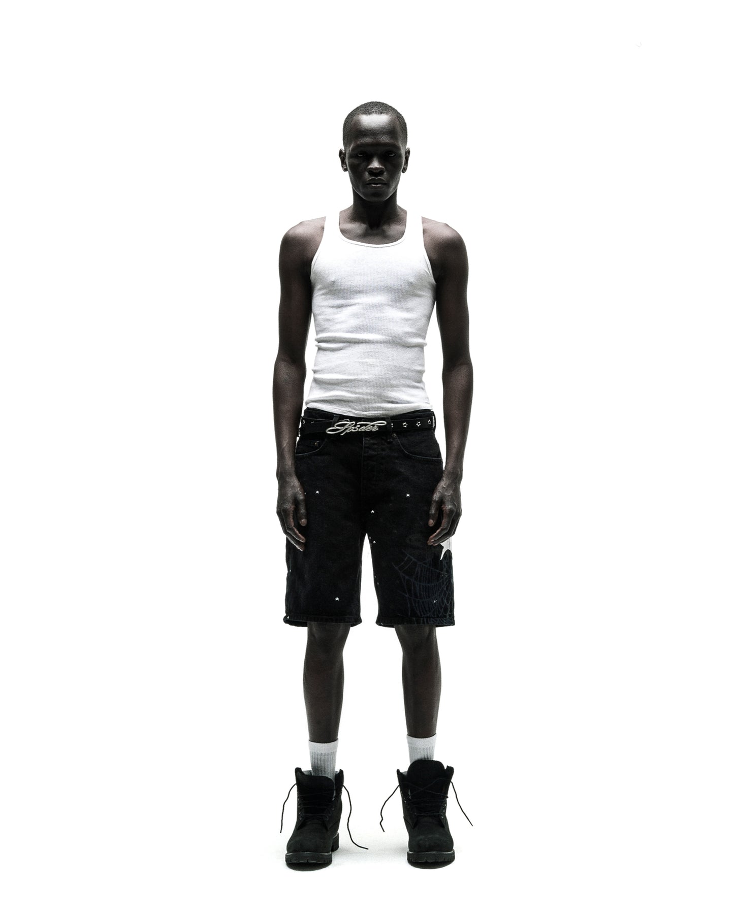 Man in black HEAVY WEB JEAN SHORTS with white web graphic, white tank top, and black boots.