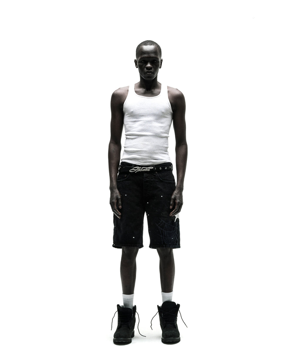 Man in black HEAVY WEB JEAN SHORTS with white web graphic, white tank top, and black boots.