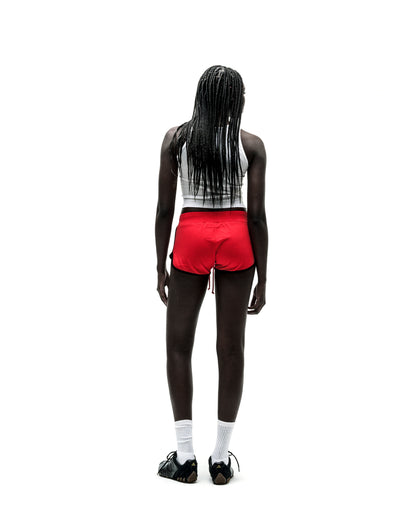 Woman in red SP5 WIDE BOXER shorts with black trim, white tank top, and black sneakers.